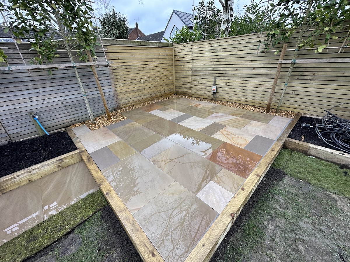 Multi tone sandstone patio with timber sleeper edging and young trees