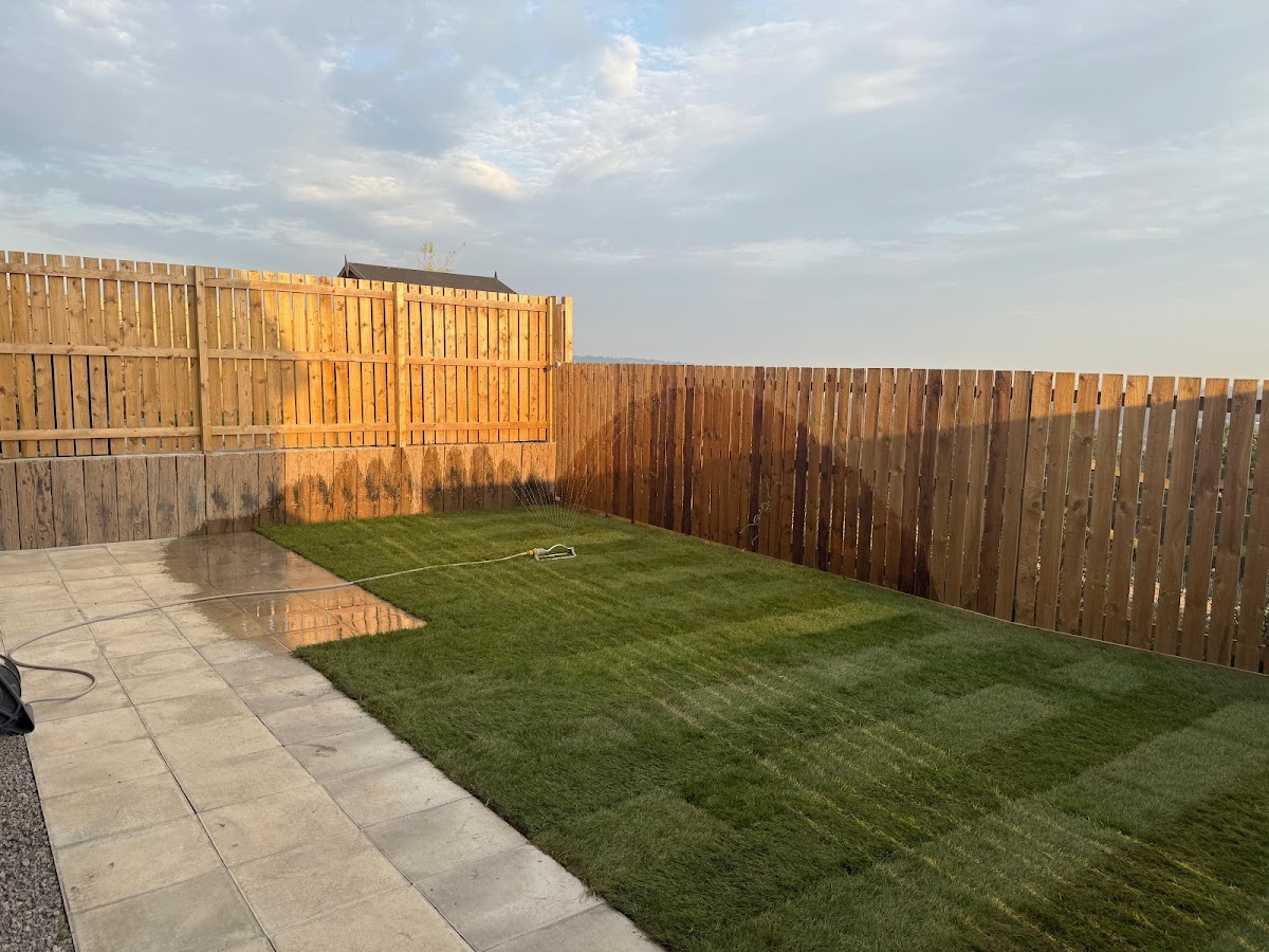 Newly laid turf being watered beside a slab path in evening light
