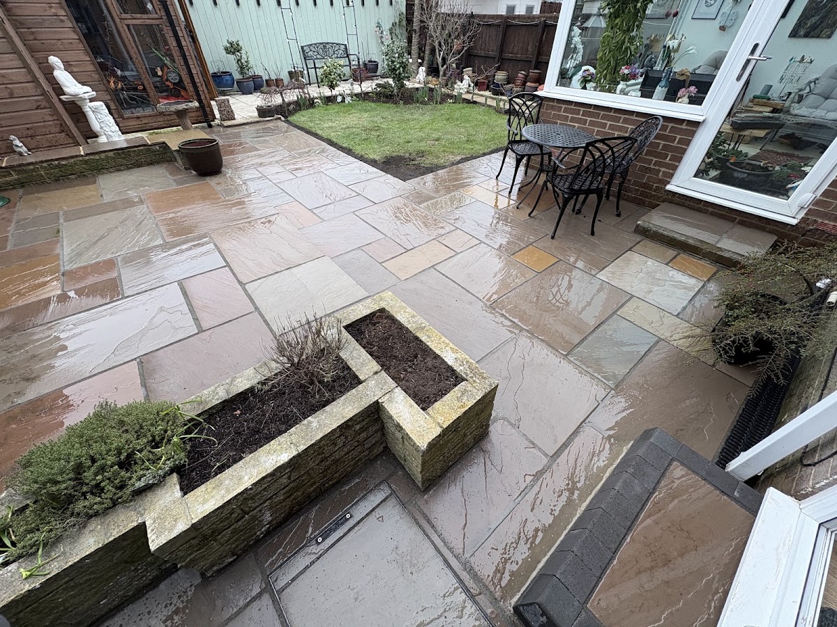 Riven sandstone patio wrapping a conservatory with a stone raised bed